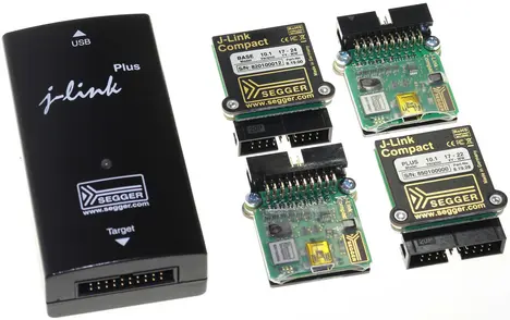 The image features a SEGGER J-Link Plus, a black USB device, alongside three J-Link Compact boards. The boards display various components and connections, designed for programming and debugging embedded systems. The products are used in electronic development environments.