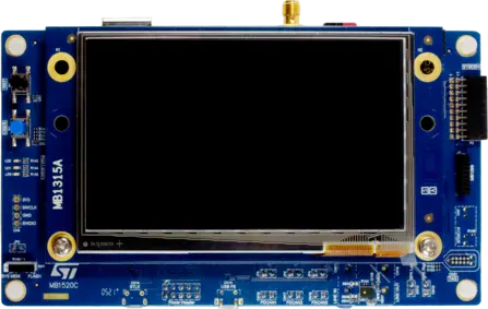 The image displays a blue electronic board featuring a central LCD screen area. Various connectors, buttons, and labeled components are visible on the edges. Notably, it includes labels such as "MB315A" and "MB1520C," suggesting it may be part of a development or display module.