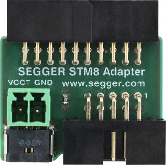 A SEGGER STM8 adapter is displayed, featuring multiple metal pins and two connection ports. The adapter includes clear labels for "VCCT" and "GND," along with the website URL "www.segger.com" printed on the green circuit board.