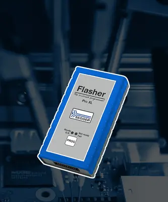 A blue and grey electronic device labeled "Flasher Pro XL" from SEGGER is prominently displayed. The device features indicators for "Ready," "Not Ready," and "Fail," suggesting its function as a programmer for electronic components. It is set against a blurred background of circuit board elements.