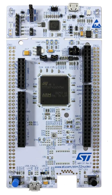The image shows a circuit board labeled as "NUCLEO" with an ARM microcontroller at the center. Various components, including connectors, resistors, LEDs, and a USB port, are present across the board, providing interfaces for programming and power. The overall design is intended for development and experimentation.