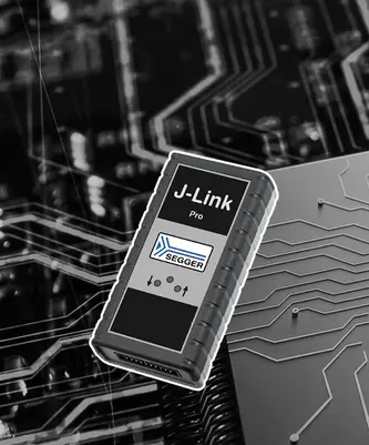 A J-Link Pro debugging tool is prominently displayed against a circuit board background. The device features a black casing with the "J-Link Pro" label and the SEGGER logo, along with control icons for functionality. It is designed for programming and debugging embedded systems.