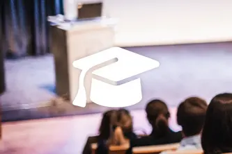 An audience is seated in a lecture hall, facing a presenter and a podium. In the foreground, a graduation cap symbol is overlaid, emphasizing the educational theme of the event. The setting suggests a focus on learning and academic achievement.
