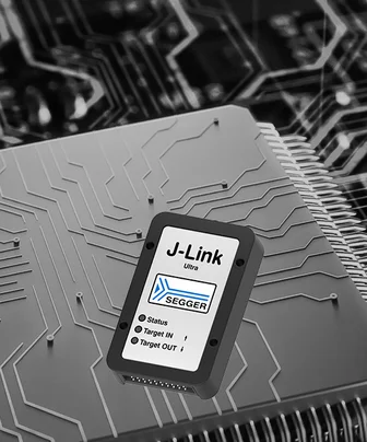 The image features a J-Link Ultra+ programming tool, prominently displayed against a circuit board background. The device has a sleek, black design with a white label displaying the logo "SEGGER" and control symbols, showcasing its role in electronics programming and debugging.