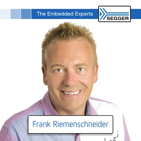 A smiling man with short, light hair is wearing a light purple shirt. Beneath him is a text box stating "Frank Riemenschneider." The background features a blue header with the text "The Embedded Experts" and a logo on the right.